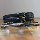 Black moose head spur straps stacked on a silver spur on wood, close-up