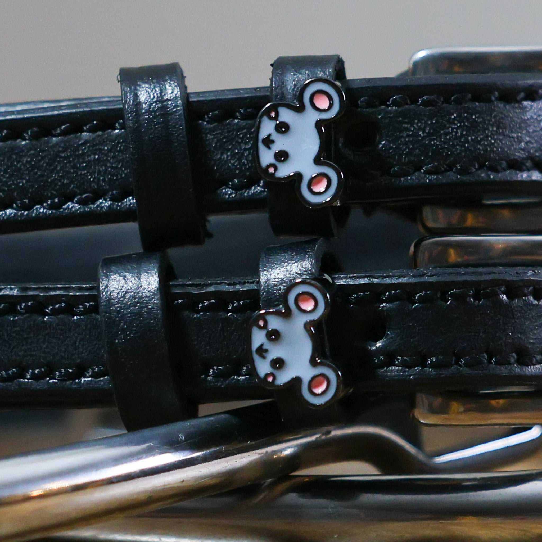Close-up of grey mouse face charms on black leather spur straps over spur hardware