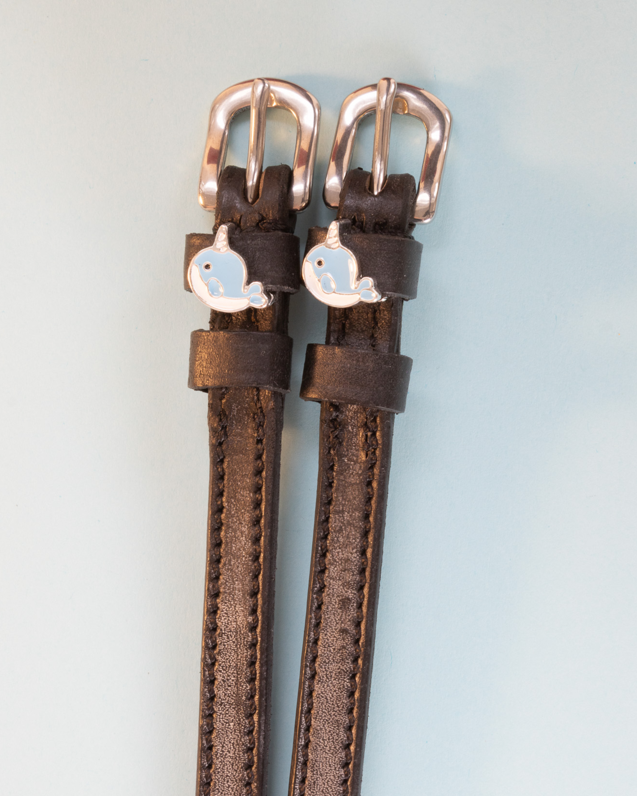 Dark brown leather narwhal spur straps with rose gold buckles on pale blue
