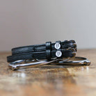 Black leather OH SH*T spur straps coiled beside a stirrup on wood