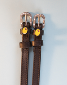 Dark brown leather olive spur straps with rose gold buckles on pale blue