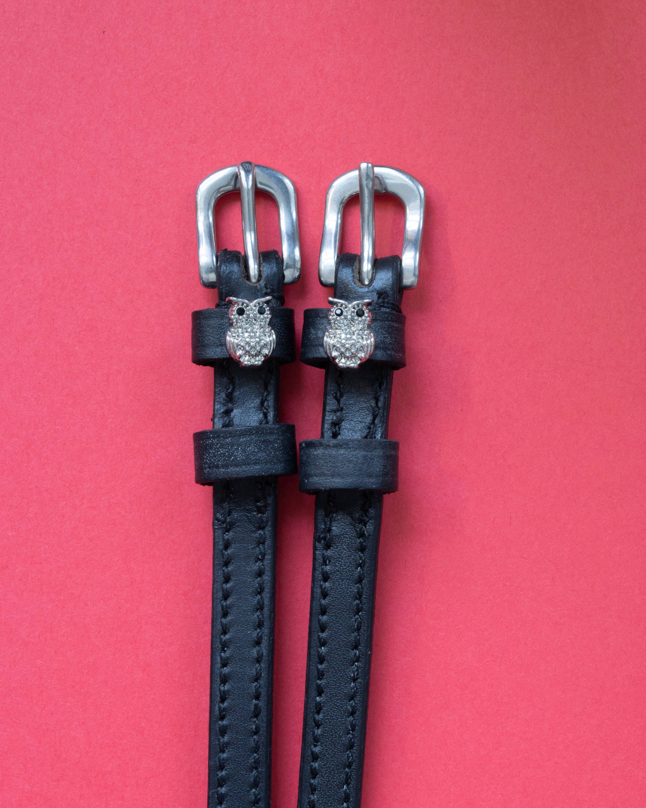 Black leather rhinestone owl spur straps with silver buckles on a red background
