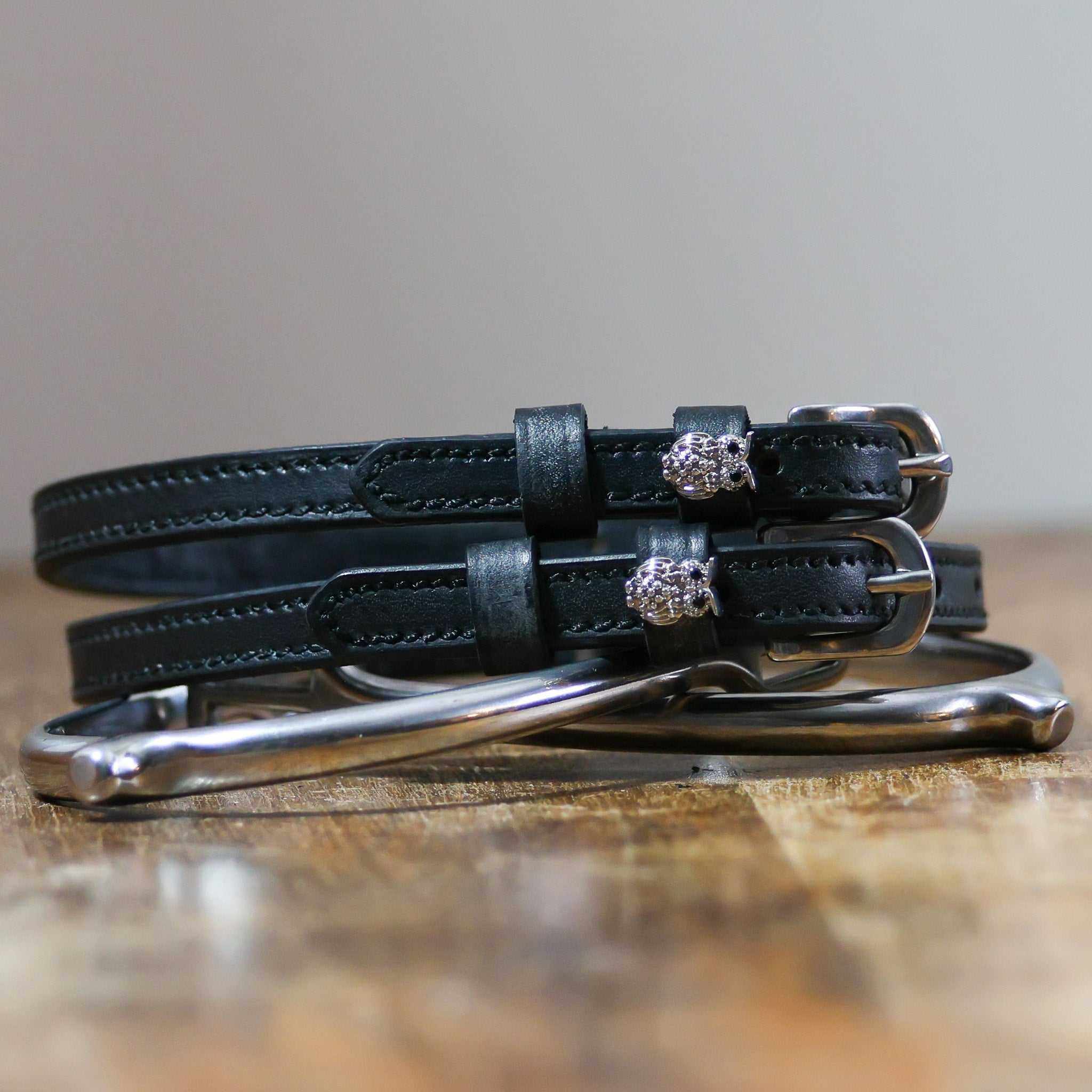 Black leather owl bling spur straps coiled beside a silver spur on a wood surface