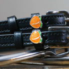 Close-up of a sparkly orange peach charm on a black leather spur strap keeper