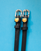 Pair of black leather peach charm spur straps on a light blue background