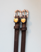 Dark brown leather ManeJane peach spur straps with rose-gold buckles on grey