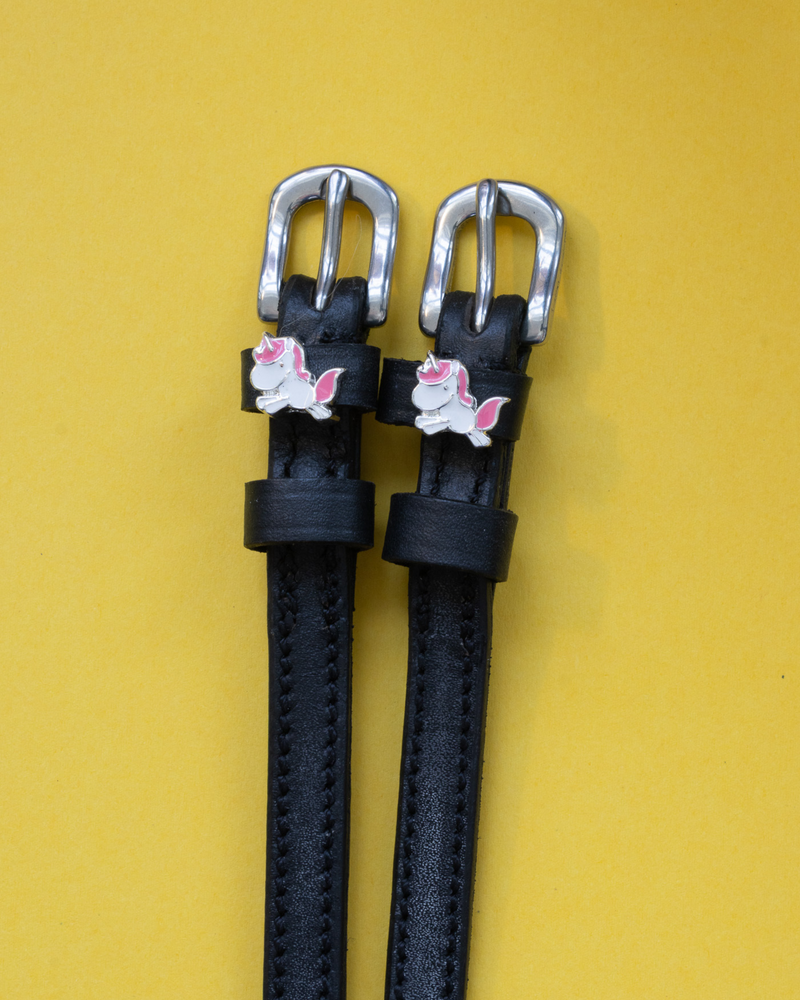 Black leather ManeJane spur straps with silver buckles and chubby unicorn charms on yellow