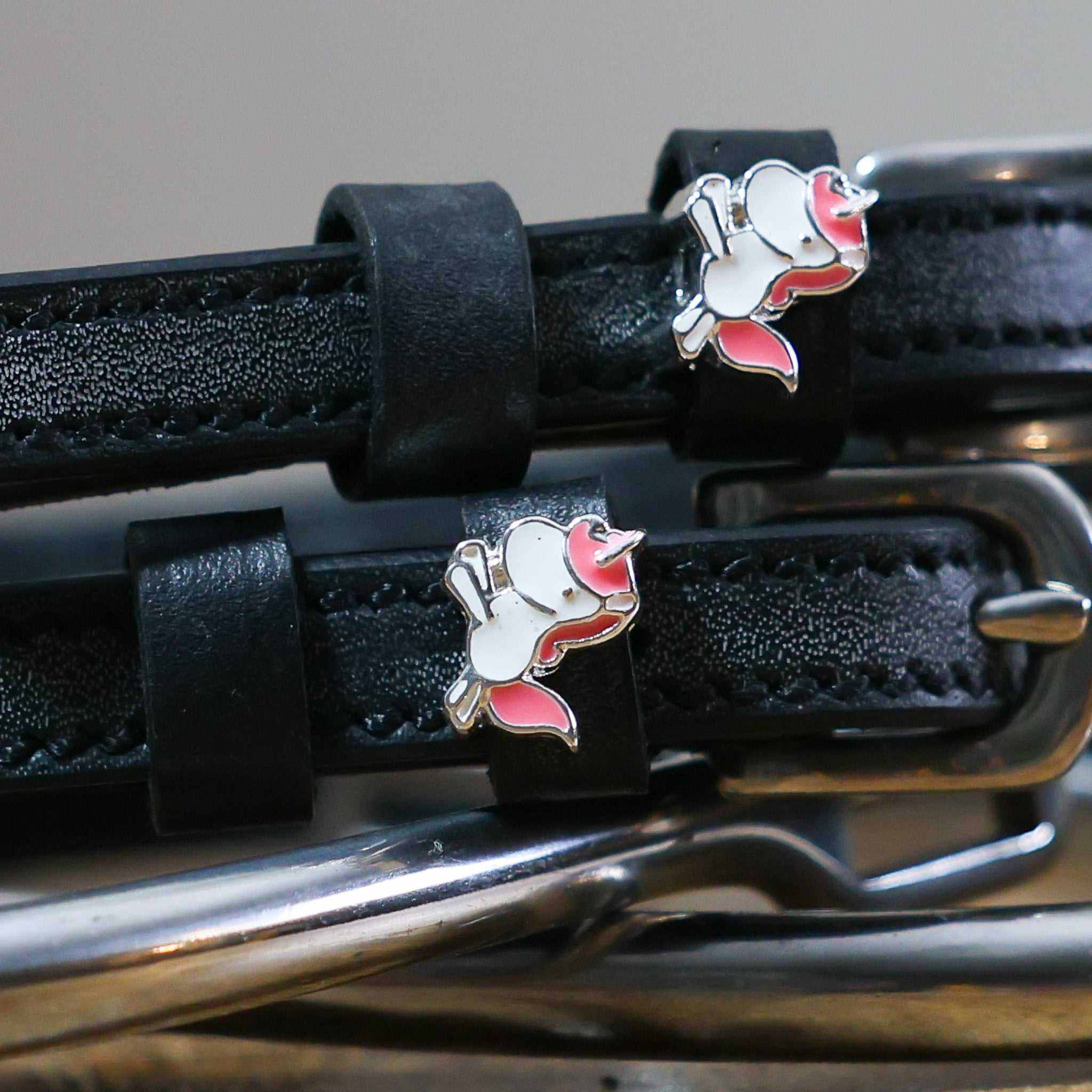 Close-up of white-and-pink unicorn charms on black leather spur strap keepers