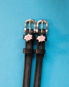 Black leather winged pig charm spur straps on a bright blue background