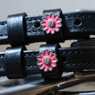 Close-up of pink daisy charms with rhinestone centers on black leather spur straps
