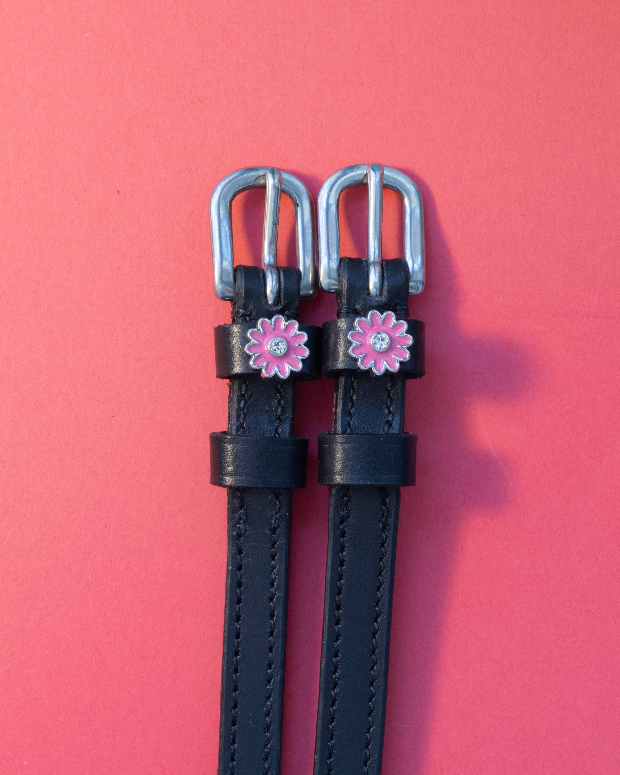 Pair of pink flower spur straps with silver buckles laid flat on a coral background