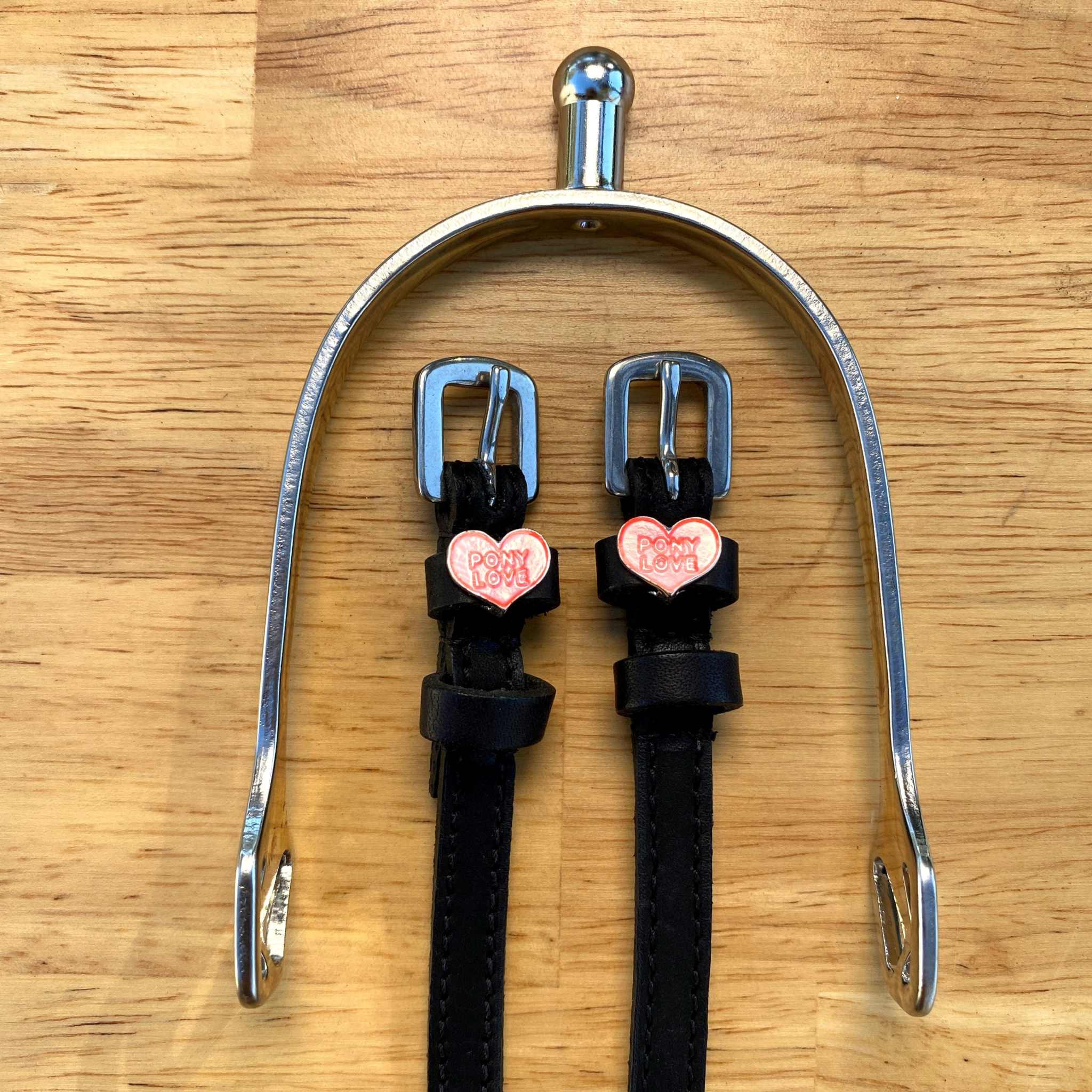Pony Love spur straps hung from a silver spur bracket on a wood surface
