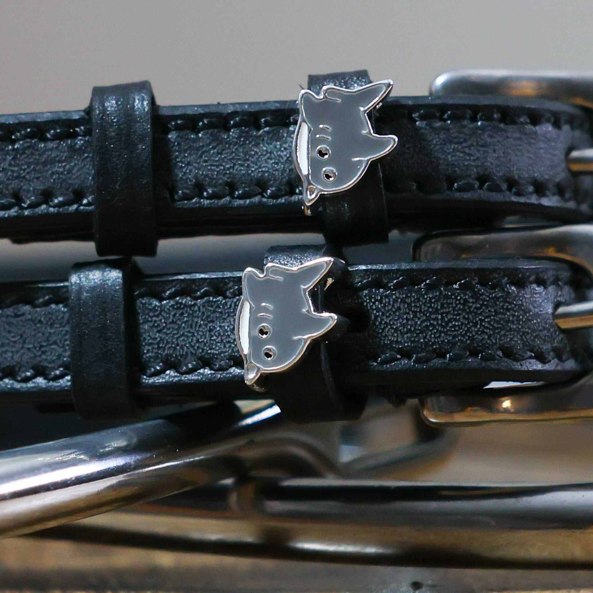 Close-up of silver shark charms on black leather spur strap keepers with hardware