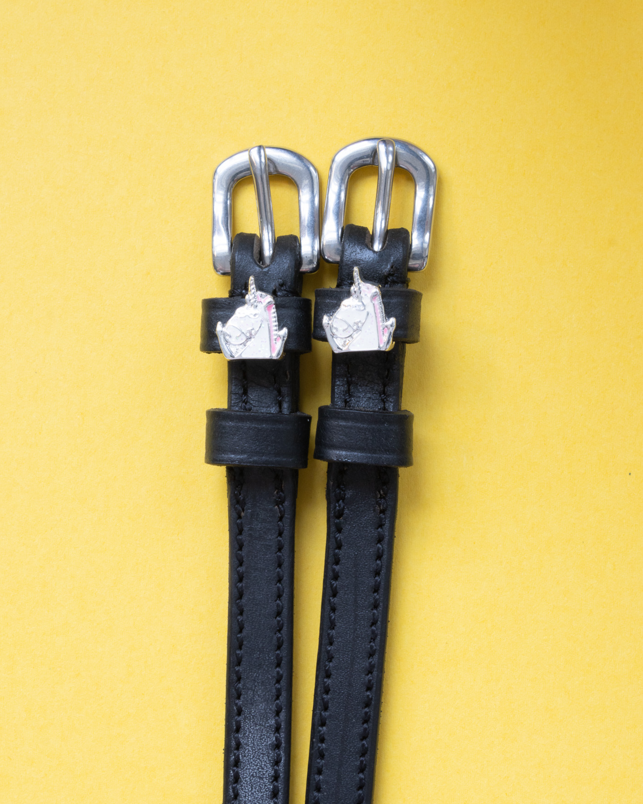 Black leather ManeJane spur straps with silver unicorn head charms and buckles on yellow