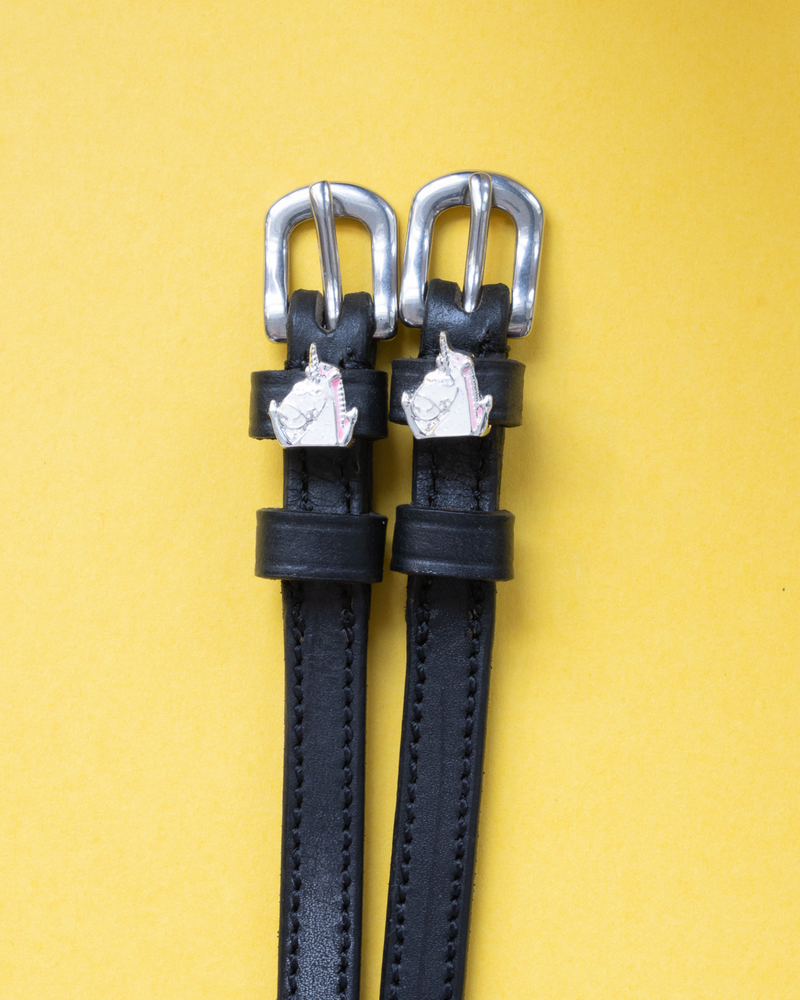 Black leather ManeJane spur straps with silver unicorn head charms and buckles on yellow