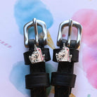 Silver unicorn head charms on black leather spur straps over a pastel watercolor background
