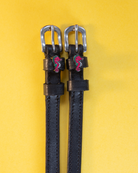 Pair of black leather seahorse spur straps flat-laid on a yellow background