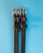 Black leather ManeJane seahorse spur straps on a bright blue background
