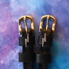 Close-up of rhinestone lightning bolt charms on black spur straps over a galaxy backdrop