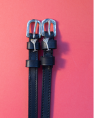 Black leather ManeJane spur straps with silver martini glass charms flat-laid on coral