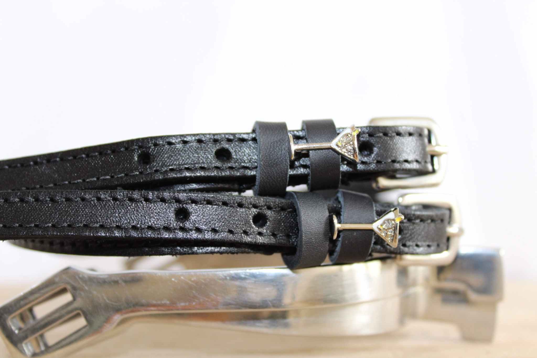 Black martini glass spur straps resting on a polished silver spur, close-up