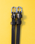 Pair of black leather martini glass spur straps laid flat on a yellow background