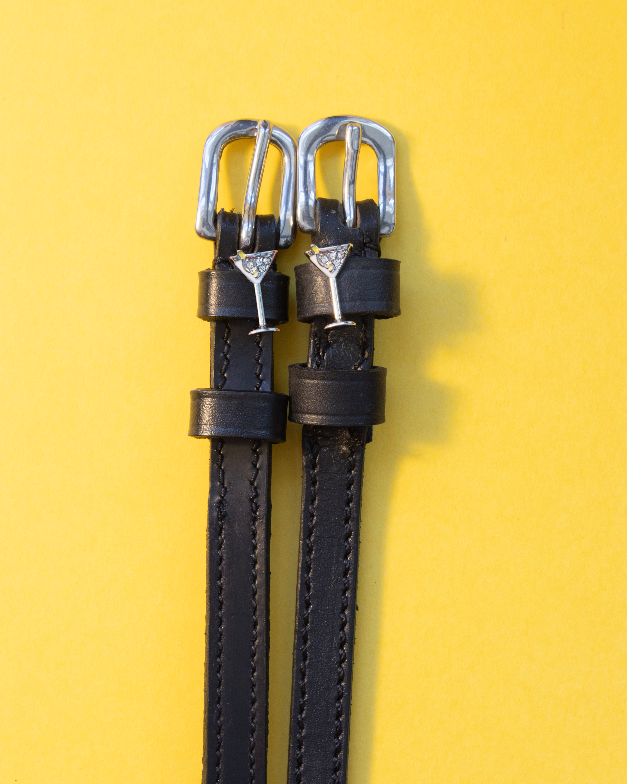 Pair of black leather martini glass spur straps laid flat on a yellow background