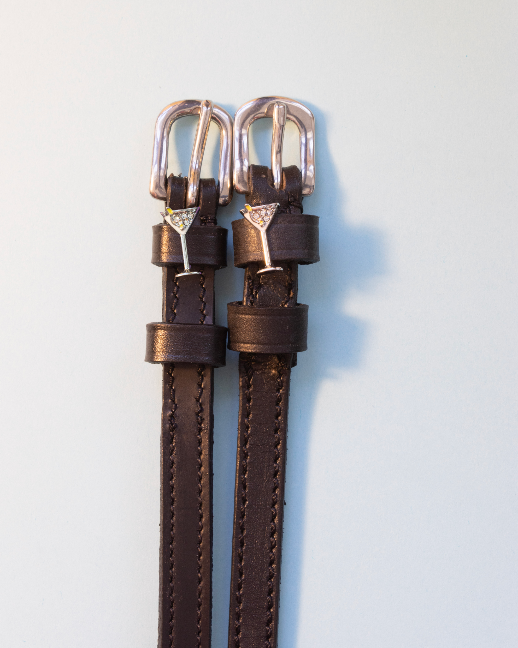 Dark brown leather martini glass spur straps with silver buckles on off-white