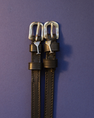 Black leather martini glass spur straps flat-laid on a deep purple background