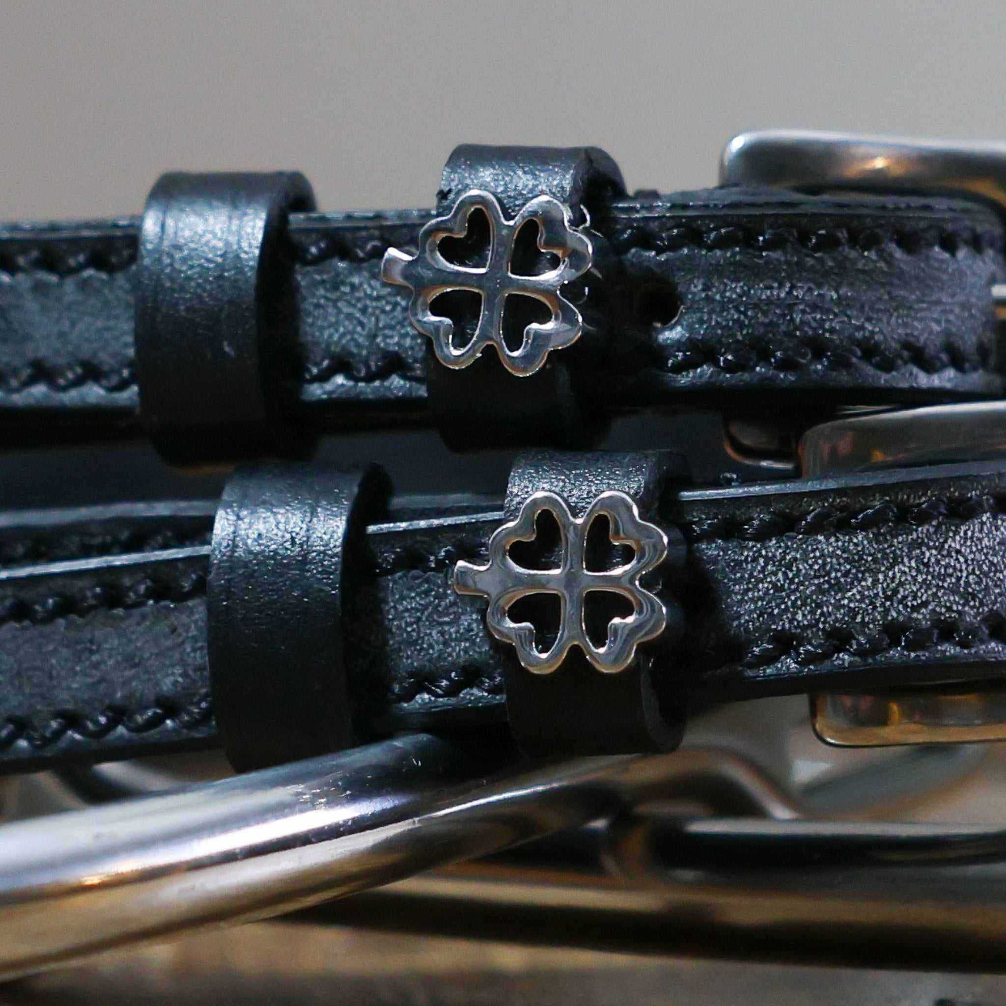 Close-up of silver outline clover charms on black leather ManeJane spur straps