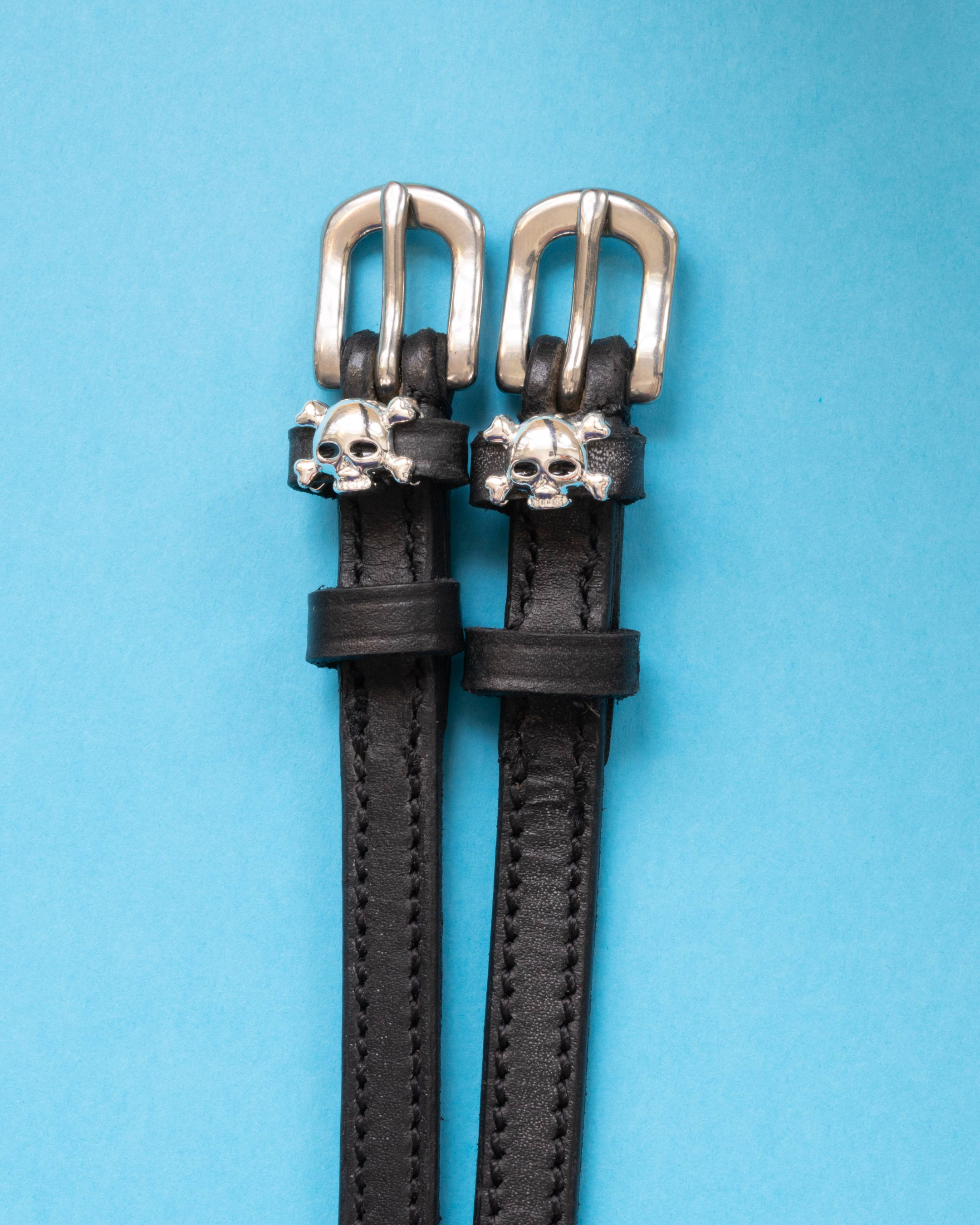 Pair of black leather skull and crossbones spur straps with silver buckles on bright blue
