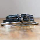 Black leather skull and crossbones spur straps coiled beside a silver spur on wood