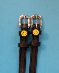 Brown leather ManeJane spur straps with yellow smiley-face charms on blue
