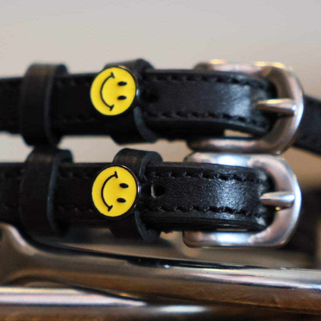 Close-up of yellow smiley-face charms on black leather spur strap keepers