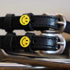 Close-up of yellow smiley-face charms on black leather spur strap keepers