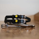 Black leather smiley spur straps coiled on wood beside a stirrup