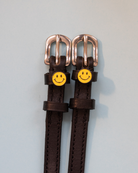 Brown leather spur straps with smiley-face charms and rose-gold buckles