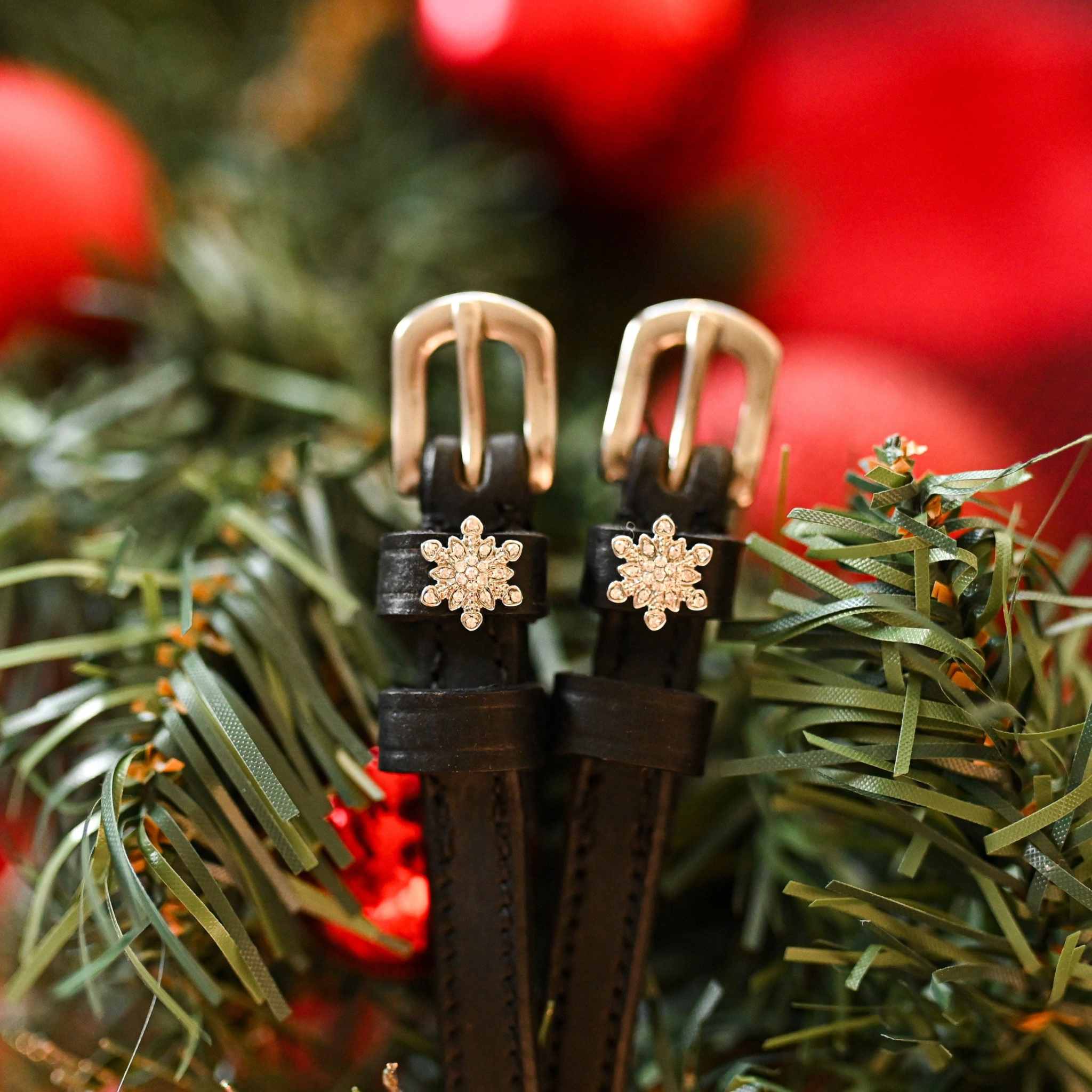 Snowflake spur straps with rose-gold buckles nestled in a pine Christmas wreath, ManeJane