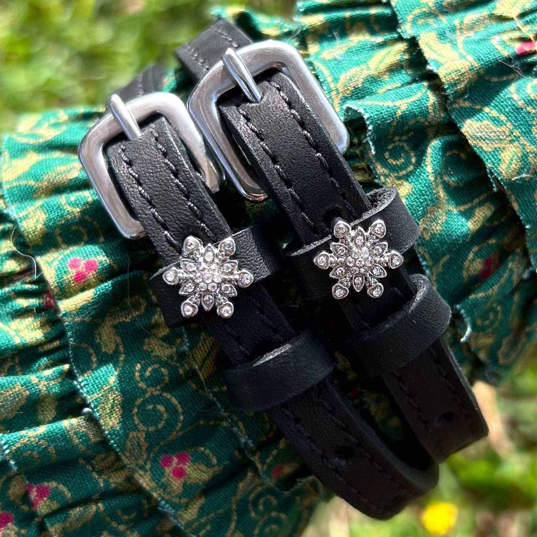 Snowflake spur straps with crystal charms draped over green floral fabric, ManeJane