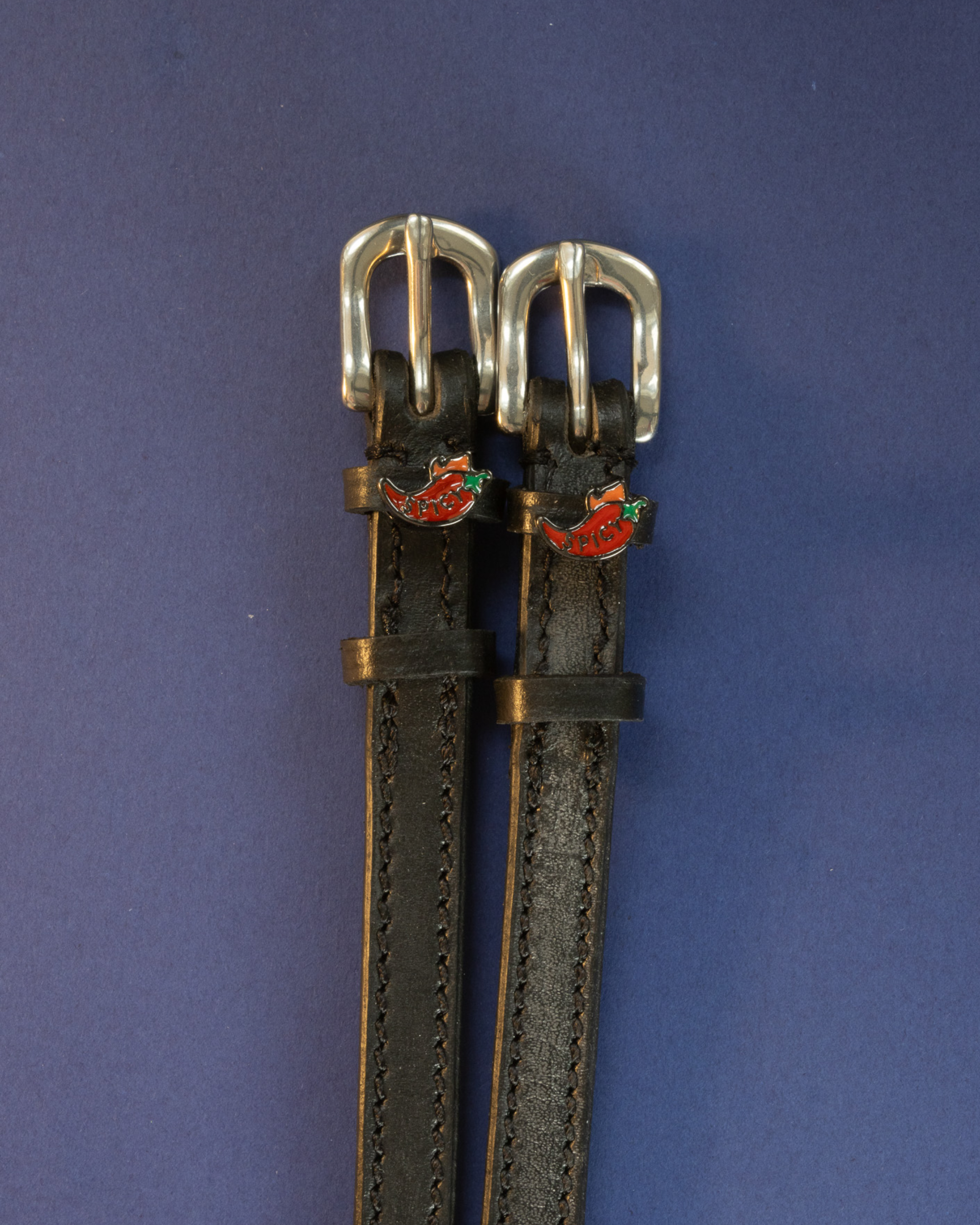Black leather chili pepper ManeJane spur straps with silver buckles on a navy background