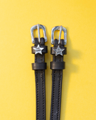 Pair of black leather Boss star spur straps flat-laid on a yellow background