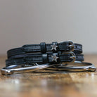 Pair of black leather Boss star spur straps coiled on wood beside a silver bit