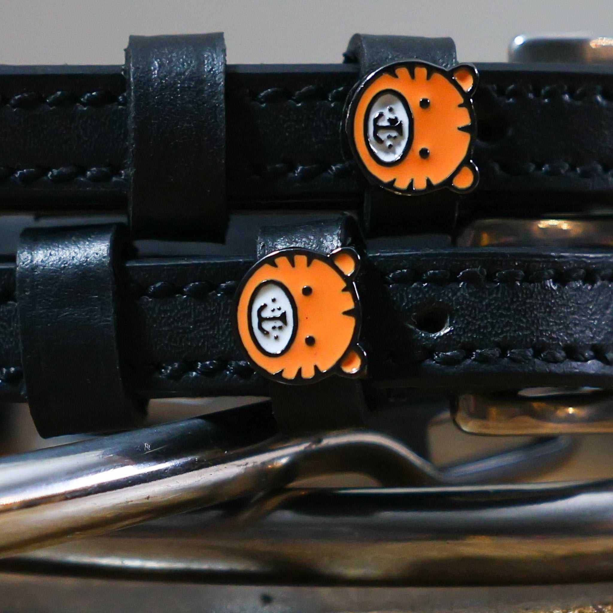 Close-up of orange tiger-face charms on black leather spur strap keepers