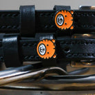 Close-up of orange tiger-face charms on black leather spur strap keepers