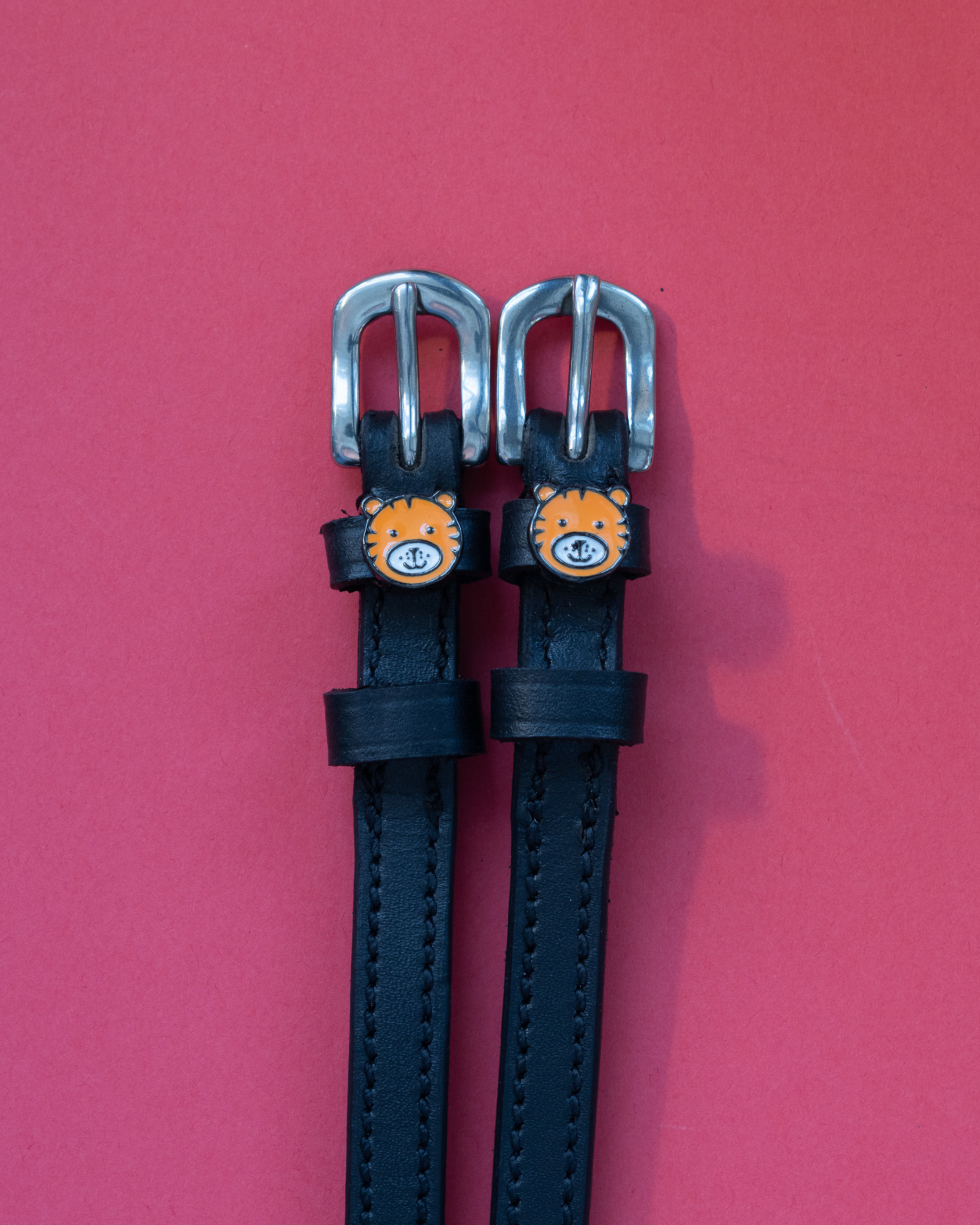 Black leather tiger-face spur straps with silver buckles on a red background