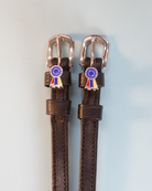 Dark brown leather rosette ribbon spur straps with rose gold buckles on pale blue