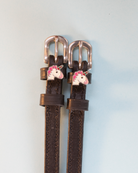 Dark brown leather unicorn spur straps flat-laid on a soft blue-grey background