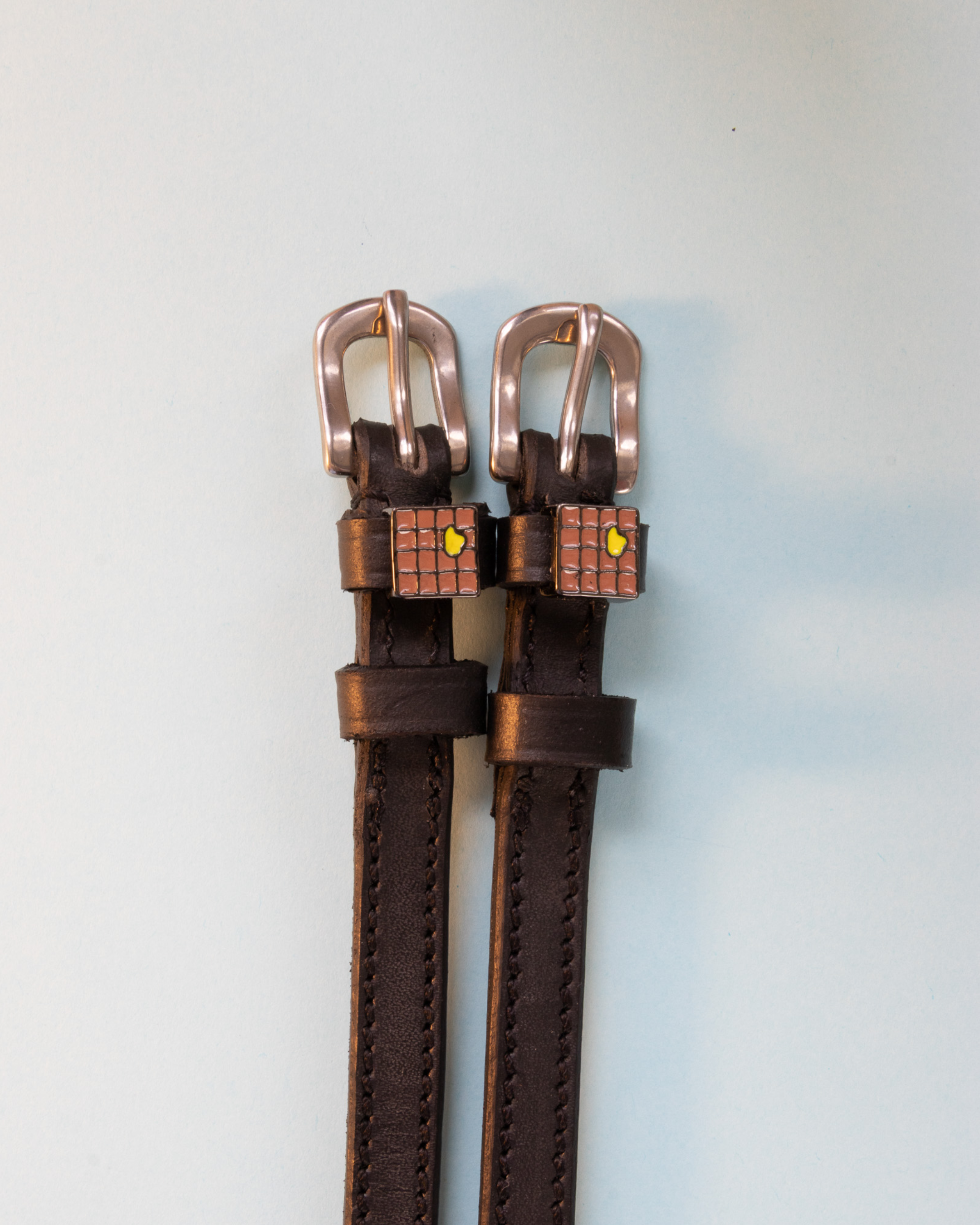 Brown leather spur straps with waffle charms and rose-gold buckles