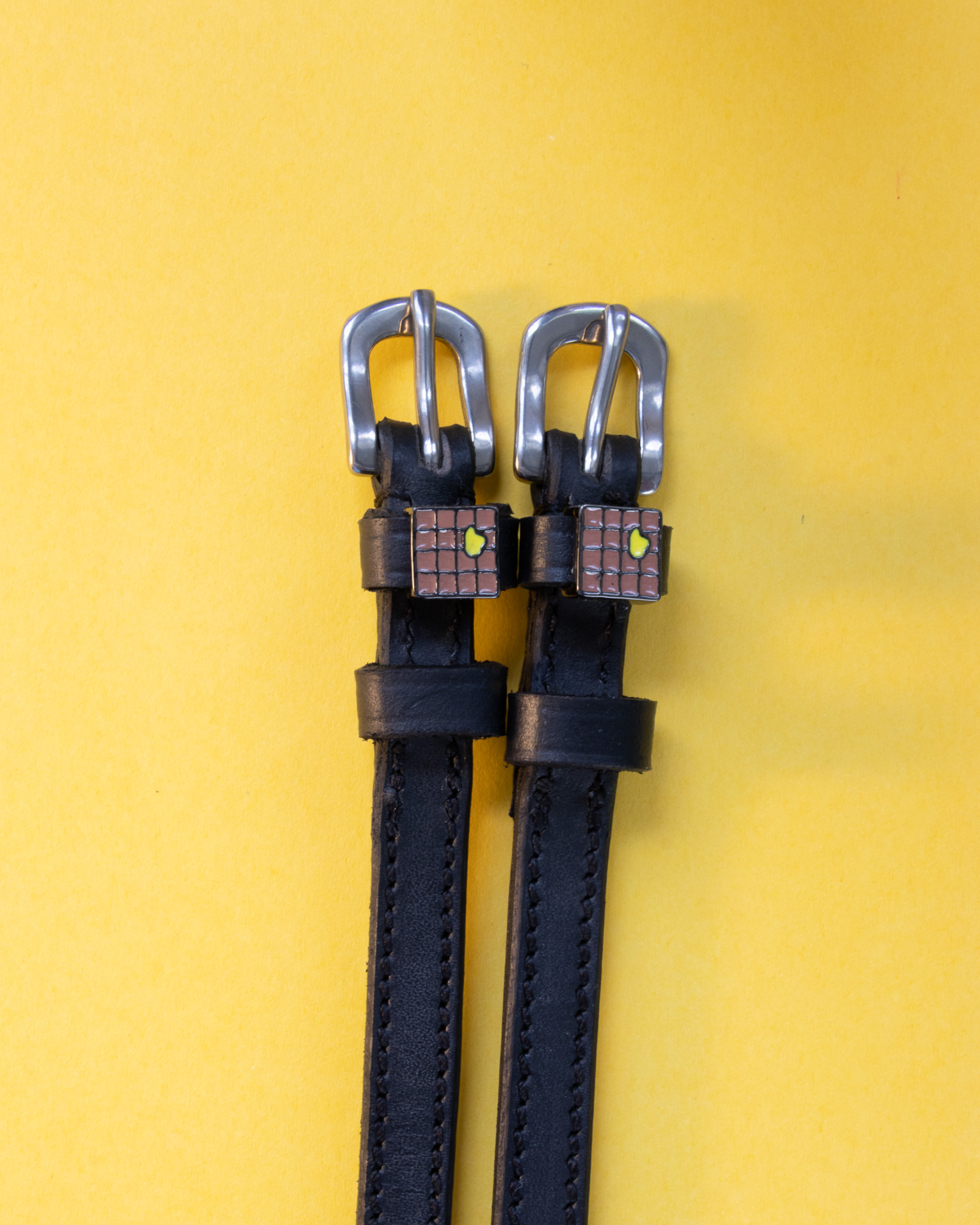 Pair of waffle-charm spur straps laid flat on a yellow background