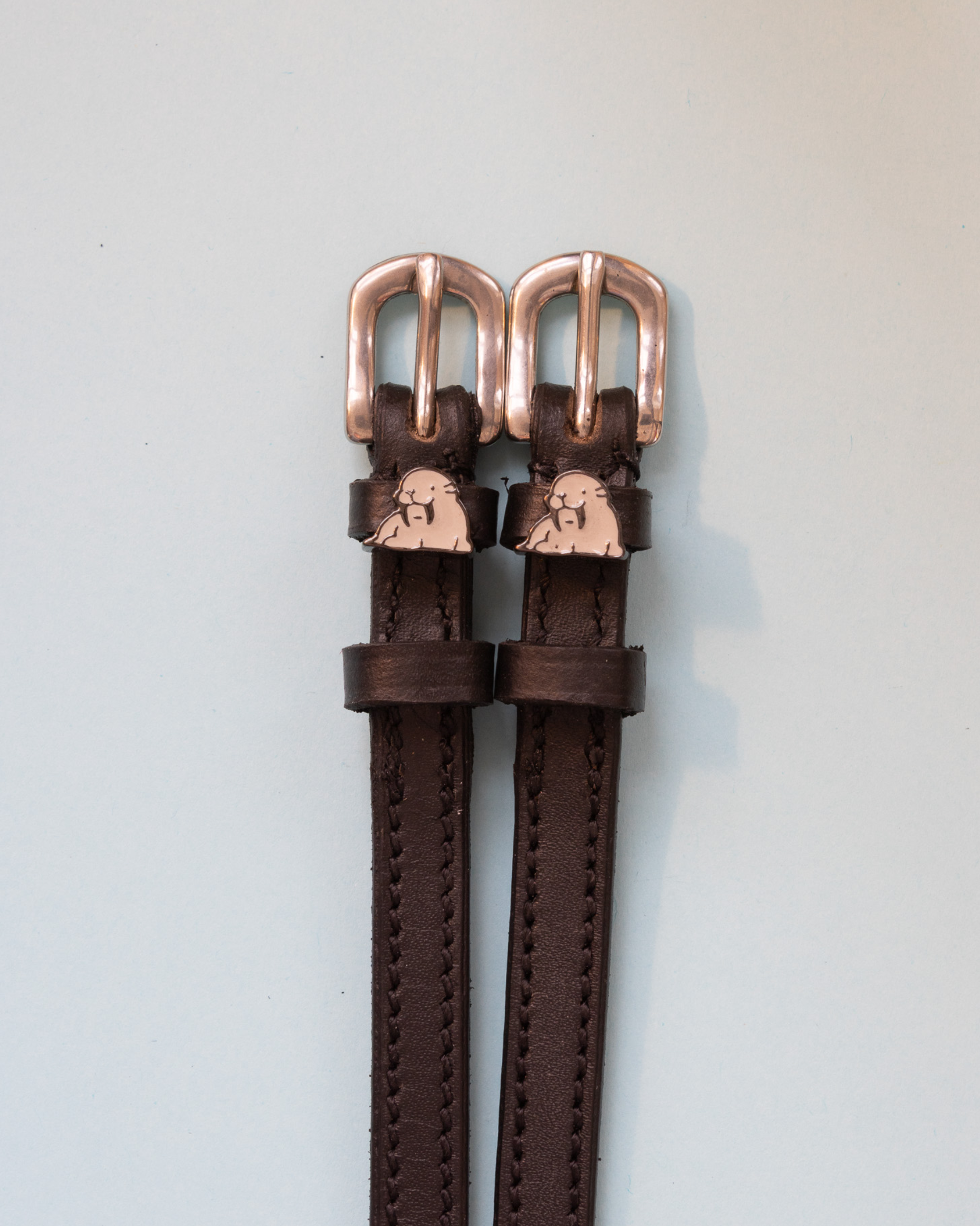 Close-up of grey walrus charms with tusks on black leather ManeJane spur strap keepers